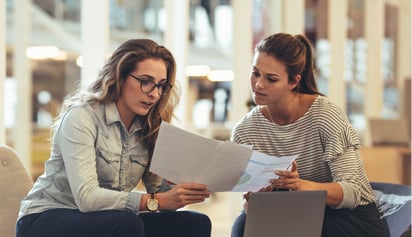two women holding papers and discussing