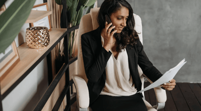 Woman on the phone holding papers sitting in a chair in her living room