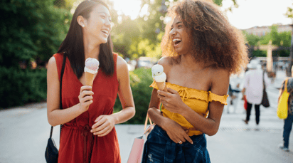 Two young women walking down a street laughing and eating ice cream
