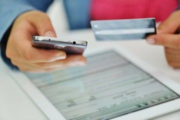 Human hands holding a smart phone and a credit card with a tablet on a desk