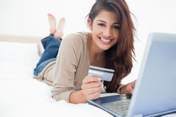 A woman smiling and looking in front of her as she uses her credit card with her laptop.