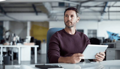 man wearing a sweater holding an ipad and looking into the distance