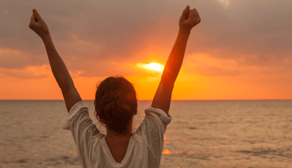 woman looking at the sunset with her arms up