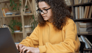 woman with curly hair and glasses typing on her laptop