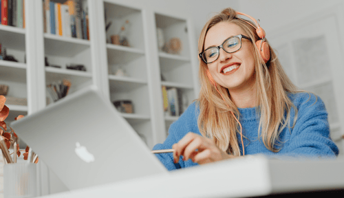 Woman wearing glasses and headphones looking at her laptop and smiling