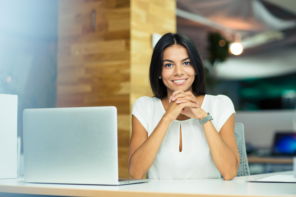 Portrait of a cheerful businesswoman sitting at the table in office and looking at camera-1
